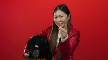 Woman pointing with a playful gesture holding helmet against vibrant red background, wearing...
