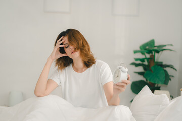 Frustrated woman sitting in bed, screaming at alarm clock after waking up late. Concept of stress,...