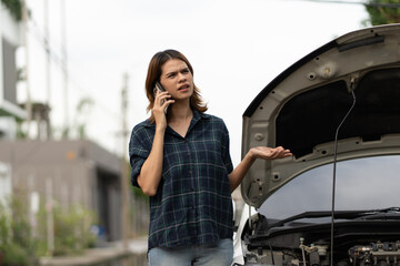 Frustrated woman calling for help while looking at a smoking car engine, representing car breakdown, roadside emergency, auto problem, vehicle failure, and need for assistance.