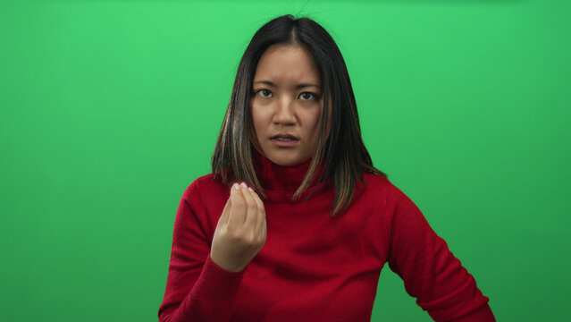 Young woman in red sweater making an expressive gesture with her hand against an isolated green background wall, conveying emotion and focus.