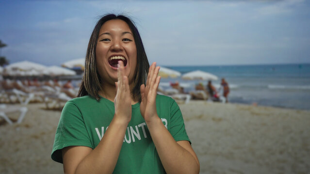 Young woman volunteer wearing green t-shirt on a seaside beach with others in the background, expressing diverse emotions against a backdrop of sand and ocean waves. - Powered by Adobe