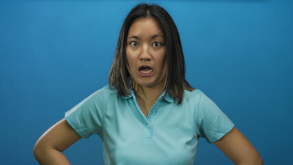 Woman expressing surprise over a blue isolated wall backdrop, wearing a light blue shirt,...