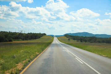 Fototapeta premium Endless sandy country road through the beautiful landscape of the Namibian Kalahari Desert during the rainy season. On a beautiful, sunny day with blue skies. Tourism and vacation concept. Namibia, Af
