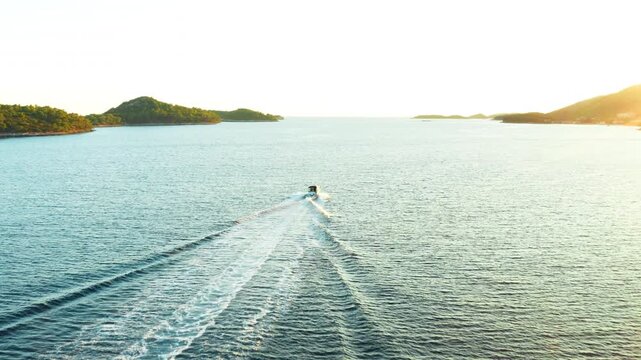 A speedboat journeys through a scenic island archipelago at sunrise or sunset in an epic aerial drone shot. The golden hour light reflects on the water, creating a mood of freedom and adventure.