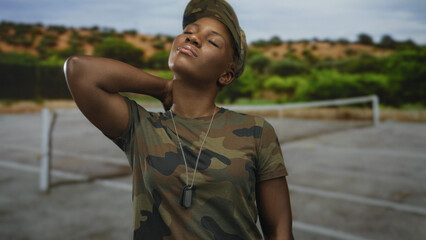 Woman soldier in camouflage uniform holds dog tags and rests hand on neck on sunlit street; calm...