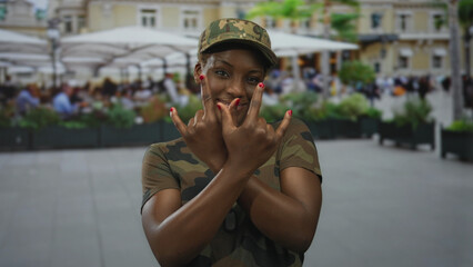 Woman soldier in camouflage uniform shows dogtag and makes rock horns gesture on street outside a...