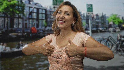 Fototapeta premium Middle aged hispanic woman gives double thumbs up gesture on street; confidence encouragement optimism.