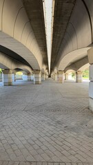 Under the Bridge: A captivating perspective of a modern bridge, showcasing its structural elegance, clean lines, and geometrical patterns under the strong midday sunlight. 