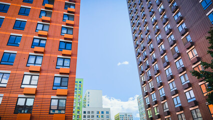 Fototapeta premium Colorful modern high-rise residential buildings with geometric facades and balconies against blue sky, representing contemporary urban architecture, housing development, and real estate investment