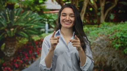 Woman makes ok sign with her hands in green park walkway among lush shrubs and palm trees under...