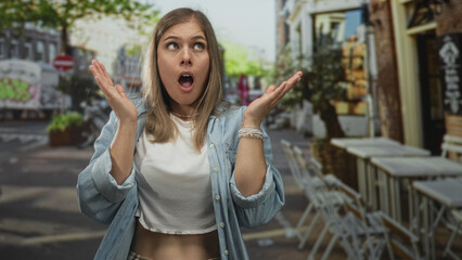 Woman pressing hands to cheek gesture on street terrace with urban cafe seating and blurred...