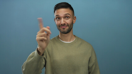 Fototapeta premium Young man gesturing with finger against blue background, wearing casual sweater, expressing serious emotion in studio setting highlighting unique facial expression