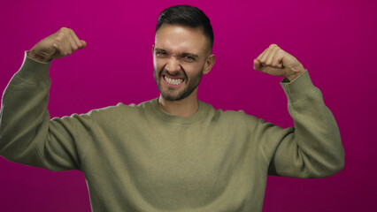 Young man flexing muscles confidently against a bold pink background, showcasing happiness and strength.