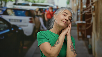 Senior woman with grey hair and tattoos stands peacefully with eyes closed on a busy city street,...