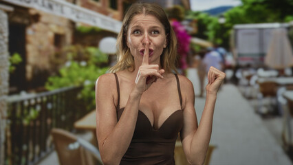 Woman showing cleavage, finger to lips for silence on a street cafe terrace restaurant outdoors,...