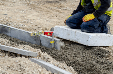 Close-up of construction worker leveling concrete and placing edging pin kerb on construction site