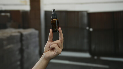 Hand holding dropper bottle indoors at a construction site, showcasing male skin tone and implying...