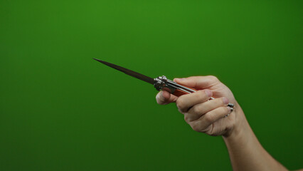 Man holding knife with isolated green background, highlighting the sharp metal blade in a gripping...