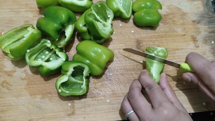 Closeup video of slicing fresh green capsicum with a knife on a wooden cutting board in the kitchen with selective focus. - Powered by Adobe