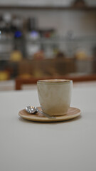 Coffee cup with spoon on saucer placed on table in cozy indoor restaurant setting with blurred background.