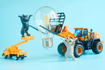 Toy forklift and truck with funny cat figurines install LED light bulb, symbolizing energy saving, electrification, and learning play for kids. Photo