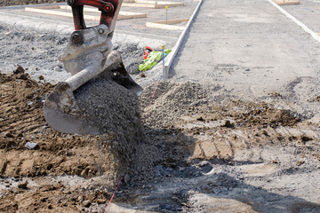 Excavator working on sidewalk installation at a residential area placing concrete around new edging pin kerb