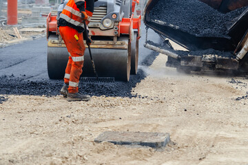 Construction workers in high-visibility gear are applyin gfresh hot asphalt to roadway surface