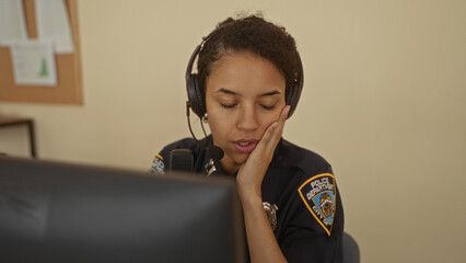 Woman officer in a police station wearing a uniform and headset, appearing focused while sitting...