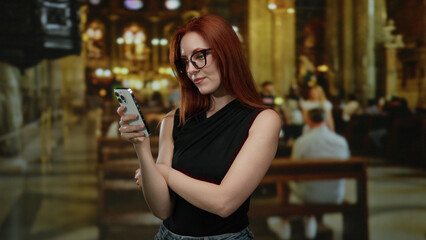 Woman with red hair using her smartphone indoors at a church, displaying a serene expression in a sacred environment with blurred background.