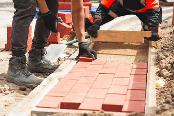 Builder laying paving bricks for footpath at construction site