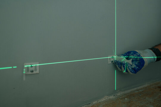 Builder repairing wall with plaster using laser level indoors