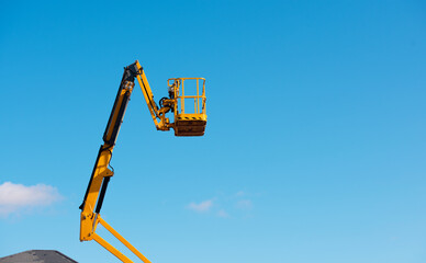 Elevated boom lift platform cherry picker against clear blue sky during daytime works on construction site with bright sunlight illuminating the machinery