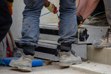 Team of builder workers lifting heavy concrete block for stairs construction. Teamwork and determination as a path to success concept.