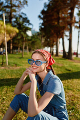 Lifestyle woman wearing modern boho-western denim street style with blue sunglasses and red bandana, smiling outdoors on a sunny day, film color effect.
