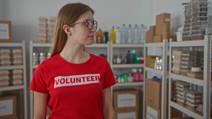 Woman wearing glasses and volunteer tshirt stands and looks ahead in a building donation space; kindness.