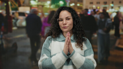 Woman smiling outdoors in busy street wearing glasses and sweater surrounded by people walking providing a vibrant urban atmosphere