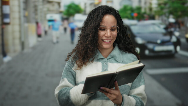 Woman smiling while reading book outdoors on bustling city street