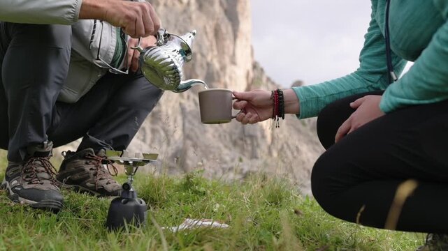 Sharing hot drink in natural setting with Ra Gusela backdrop Man pouring tea into cup held by woman in mountain field in Dolomites