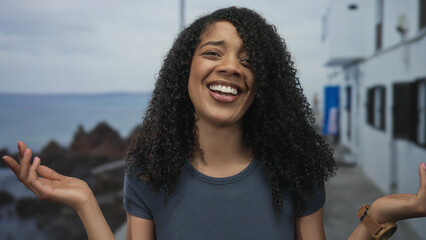 Woman in blue shirt gestures with hands on street as sea breeze blows her hair; curiosity discovery.