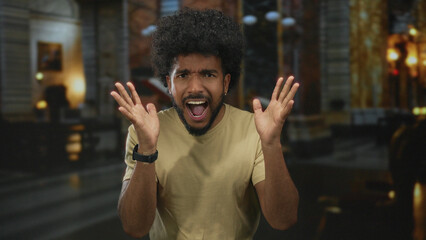 Man with an expressive face inside a church setting, displaying emotions in blurred indoor lighting.