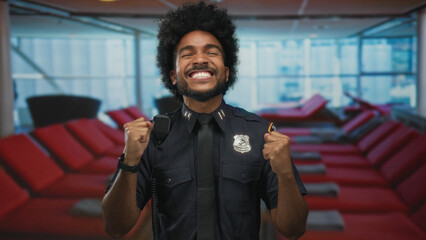 Smiling african american police officer in uniform celebrates indoors on a cruise boat with vibrant...
