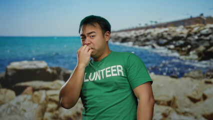 Young man at seaside wearing green shirt with volunteer text enjoying beach scenery in bright sunlight