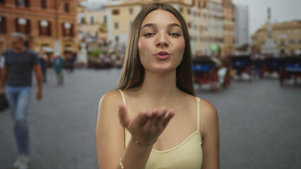 Young girl blowing kiss in historic cobblestone street under warm afternoon sunlight wearing casual...