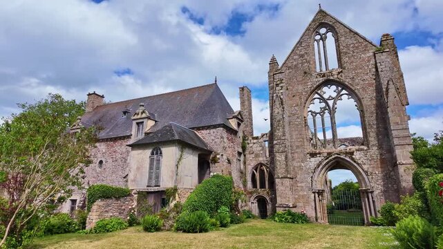Ground pan shot of Beauport Abbey ruins in Paimpol under cloudy sky with a bird landing on the top.