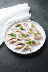 Marinated herring slices with red onion and herbs on plate with napkin on dark background