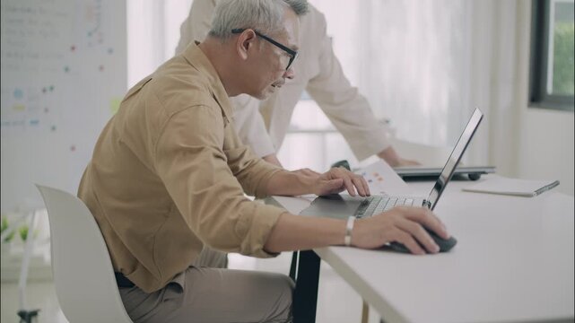 Senior Asian engineer analyzing data on laptop, typing keyboard, with colleague guidance during teamwork collaboration in a modern office environment. - Powered by Adobe