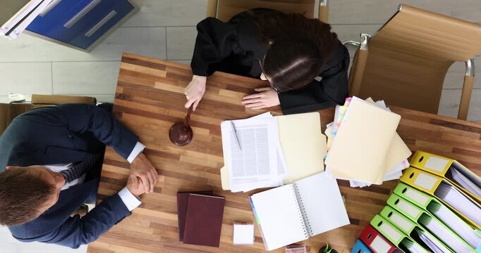 Woman judge sits at desk and raises wooden gavel to deliver decisive strike. Female listens attentively to client and makes statement. Slow motion