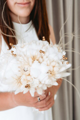 Elegant bouquet of dried flowers held by a woman in a white dress indoors