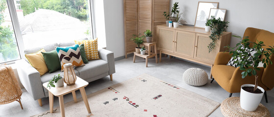 Interior of light living room with grey sofa, armchair and drawers