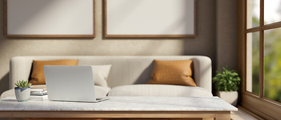 Laptop with book and pot plant on marble table across sofa with cushion aside window in living room.